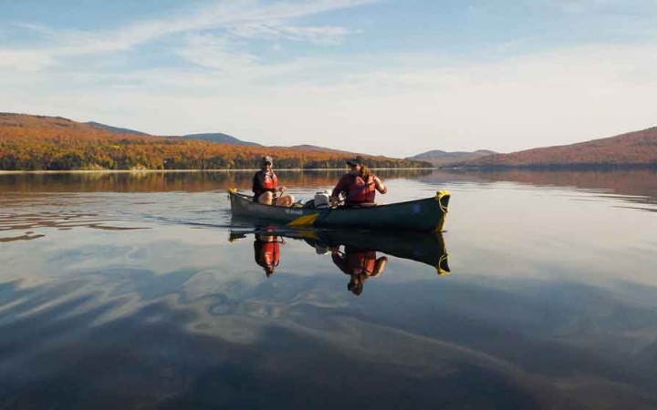 two people paddle a canoe on calm water on an outward bound expedition in maine